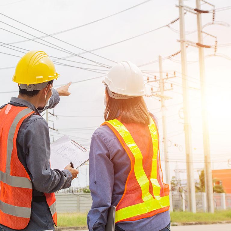 two people in hard hats pointing at electrical wires