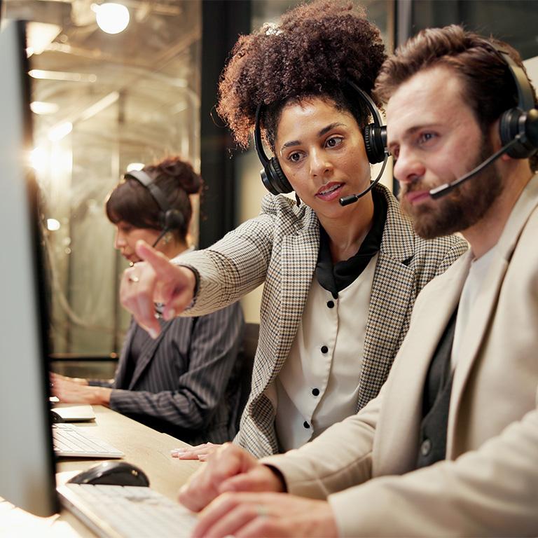 A woman at a call center with a headset on showing a man something on his computer screen